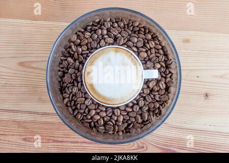 Eine Tasse Kaffee in einem mit Kaffeebohnen gefüllten Glas auf einem Holztisch Stockfoto