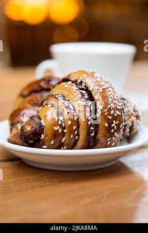 Probieren Sie Schokoladencroissant wie Rugelach und eine Tasse Kaffee auf einem Holztisch in einem Restaurant Stockfoto