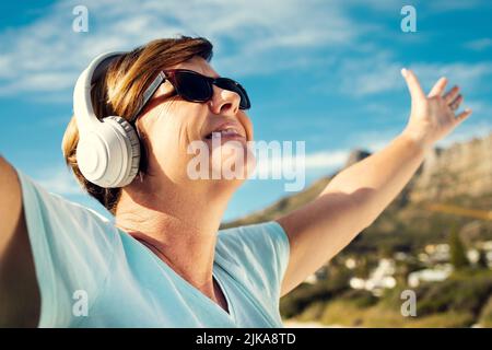 Musik ist wirklich die beste Stimmungsverbesserung. Eine Frau trägt Kopfhörer, während sie im Freien steht. Stockfoto