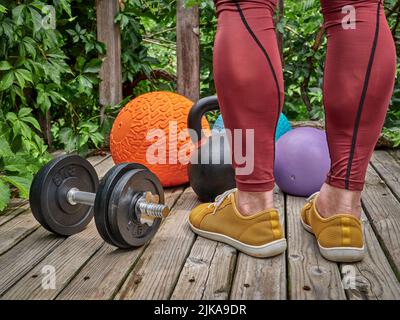 Männlich in Kompressionshose trainiert mit schweren Slam-Bällen, Hantel und Kettlebell auf einem Hinterhof-Deck, funktioneller Fitness und Hinterhof-Gym-Konzept Stockfoto