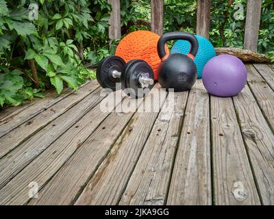 Drei schwere Slam-Kugeln, Eisen-Kugelhantel und Hantel auf einem Hinterhof-Deck, Heim- und Hinterhof-Fitnessstudio-Konzept Stockfoto