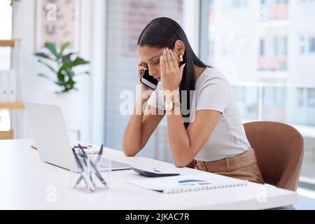 Hören Sie einfach auf zu reden und lassen Sie mich nachdenken. Eine attraktive junge Geschäftsfrau, die allein in ihrem Büro sitzt und sich gestresst fühlt, während sie ihr Handy benutzt. Stockfoto