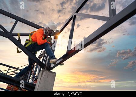 An der Dachkonstruktion arbeiten Schweißer aus Stahltraversen mit Sicherheitsvorrichtungen, um Absturzsicherheit auf der Baustelle zu verhindern. Stockfoto