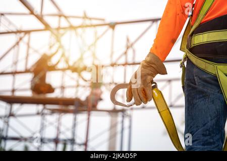 Nahaufnahme des Arbeiters auf der Baustelle, der in der Höhe der Ausrüstung arbeitet. Fallschutzvorrichtung für Arbeiter mit Haken für den Sicherheitsgurt. Stockfoto