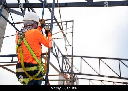 Die Arbeiter arbeiten auf der Baustelle an Stahldachstühlen mit Fallsicherung für Arbeiter mit Haken für Sicherheitsgurtzeuge. Stockfoto