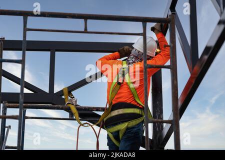 Industriestahl-Dachtraversen-Schweißer schweißen Stahl mit Fallsicherung für Arbeiter mit Haken für Sicherheitsgurt auf der Baustelle Stockfoto