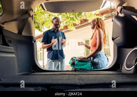 afroamerikanisches Paar, das Reisetaschen und Trolley in den Kofferraum legte und sich mit dem Auto auf den Urlaub vorbereite. Reisen mit dem Auto auf Autotour mit Gepäck und Koffern. Stockfoto