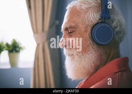 Profil eines älteren Mannes mit weißem Bart, der über kabellose Kopfhörer Musik hören kann Stockfoto