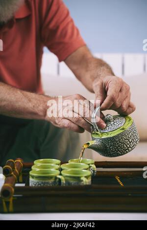 Hände eines älteren Mannes, der Tee in Tassen auf einem Bambustablett gießt Stockfoto