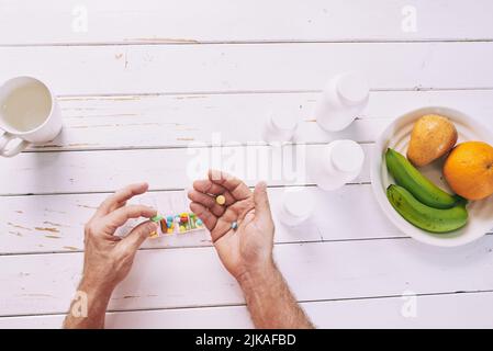Direkt über der Ansicht der Hände, die bunte Pillen aus dem Behälter nehmen, Teller mit Früchten in der Nähe Stockfoto