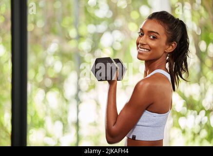 Geben Sie niemals auf ein Tor auf, nur weil es sich Zeit nehmen wird. Eine sportliche junge Frau, die im Fitnessstudio mit Hanteln ausarbeitet. Stockfoto