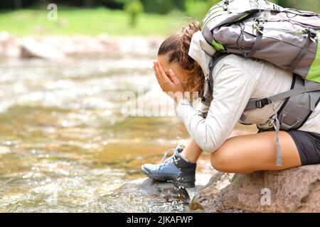 Profil einer Trekkingfrau, die Gesicht in einem Fluss im Berg putzt Stockfoto