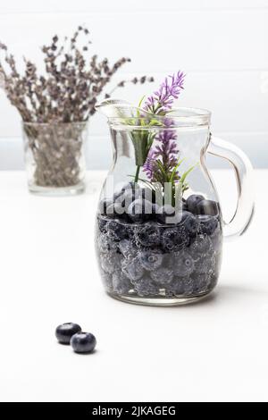 Mineralwasser mit Heidelbeere im Glasgefäß. Lavendel im Glas. Draufsicht. Weißer Hintergrund. Stockfoto