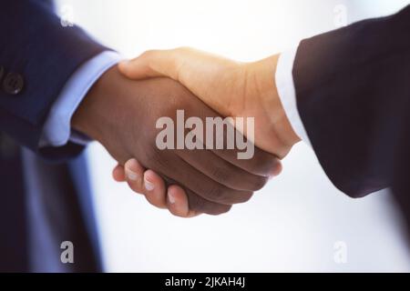 Ich bin ein seltener Verteidiger. Zwei nicht erkennbare Geschäftsleute, die sich vor einem verschwommenen weißen Hintergrund die Hände schütteln. Stockfoto