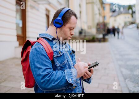 Fröhlicher junger Mann mit Down Sydrome, der Musik hört, wenn er auf der Straße läuft. Stockfoto