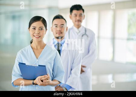 Porträt einer hübschen vietnamesischen Ärztin und ihrer Mitarbeiter dahinter Stockfoto