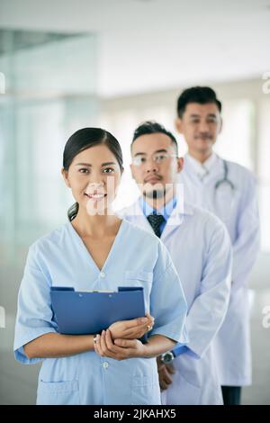 Lächelnde junge Ärztin und ihre männlichen Kollegen dahinter Stockfoto