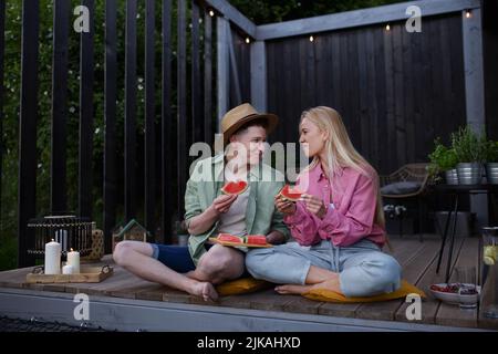 Fröhliches junges verliebtes Paar, das auf der Terrasse Wassermelone isst. Stockfoto