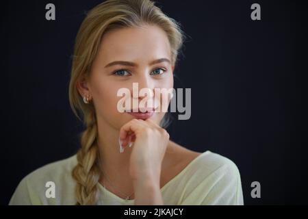 Porträt einer schönen blonden jungen Frau, die die Kamera anschaut und auf schwarzem Hintergrund lächelt, Nahaufnahme Stockfoto