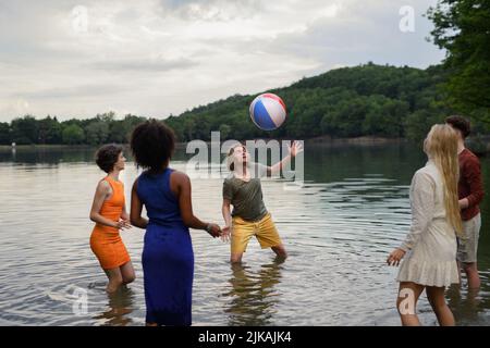 Multirassische Gruppe junger Freunde, die während des Sommers mit Ball im See spielen und Spaß haben. Stockfoto