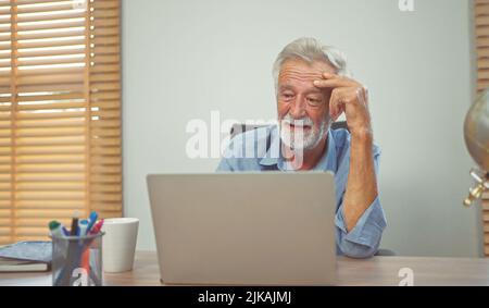 Besorgter älterer Mann, der zu Hause mit einem Laptop unterwegs war. Stockfoto