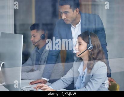 Das ist eine gute Arbeit. Ein gutaussehender, junger, männlicher Call Center-Floor-Manager, der seine Mitarbeiter im Büro überwacht. Stockfoto