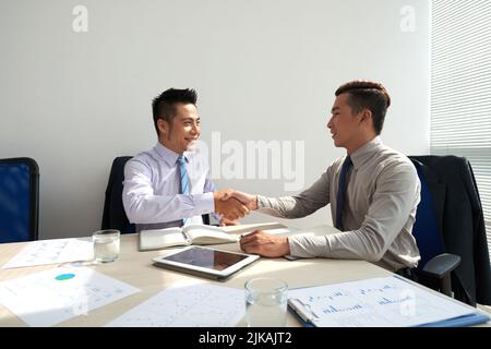 Fröhlicher asiatischer Geschäftsleiter, der nach dem Gespräch die Hände schüttelt Stockfoto