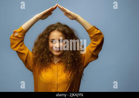 Foto-Porträt einer Frau, die Dach über dem Kopf mit Händen isoliert auf grauem Hintergrund. Lebensversicherungskonzept. Stockfoto