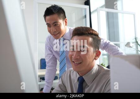 Ein fröhlicher Geschäftsmann hilft seinem Kollegen bei der Arbeit Stockfoto