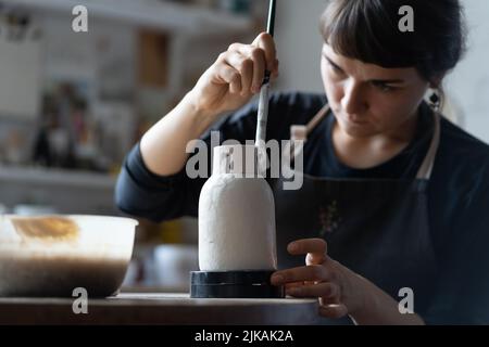 Glücklich konzentriert junge Handwerker malt Tonvase sitzen am Arbeitstisch Nahaufnahme Stockfoto