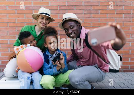 Multirassische Familie, die zusammen mit kleinen Kindern reist. Selfie vor einer Mauer. Stockfoto