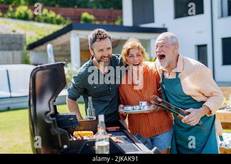 Seniorenpaar mit erwachsenen Sohn, der draußen auf dem Hinterhof in der Sommerfamilie während der Gartenparty im Freien gärt Stockfoto