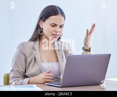 Warum habe ich so viel damit zu kämpfen. Eine junge Frau, die aufgeregt aussieht, während sie in einem Büro an einem Laptop arbeitet. Stockfoto