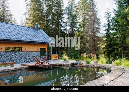 Blick auf schönes Ferienhaus mitten im Wald, umgeben von Natur mit Naturpool und Strandliegen. Stockfoto
