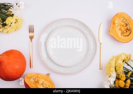 Stilvolles Tischdekor, gelbe Dahlia-Blumen, Kürbisse und Teller auf weißem Tisch. Draufsicht, flach liegend Stockfoto