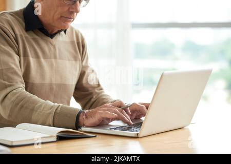 Zugeschnittenes Bild eines gealterten Geschäftsmanns, der auf einem Tablet mit einem Laptop arbeitet Stockfoto