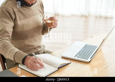 Mann mit einem Glas Wein, der Pläne in seinen Notizblock schrieb Stockfoto