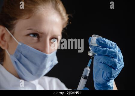 Eine Ärztin zieht einen Impfstoff oder ein Medikament in eine Spritze. Die Krankenschwester zieht den Impfstoff, die Grippemedikamente und Krankheiten in die Spritze. Stockfoto