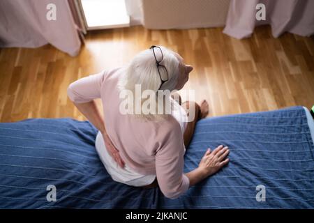 Ältere kaukasische Frau, die ihren unteren Rücken hielt und unter Schmerzen litt. Stockfoto