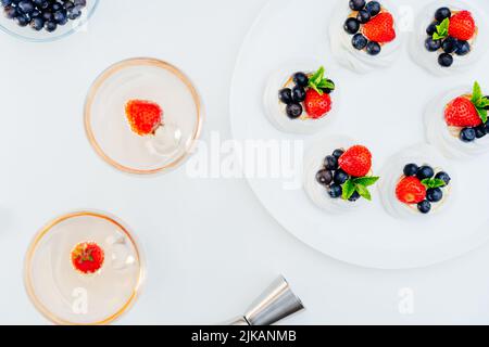 Draufsicht Meringue Pavlova Kuchen mit frischen Erdbeeren und Blaubeeren mit Minze auf dem weißen Teller und Cocktailgetränke mit Erdbeere. Desserts und Stockfoto