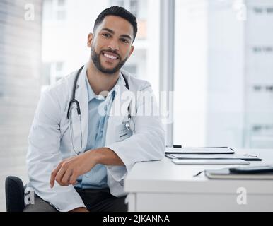 Ihre Gesundheit ist in guten Händen. Ein junger Arzt sitzt an einem Schreibtisch in einem Büro. Stockfoto