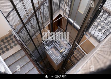 Dramatische Aufnahme eines Treppenhauses mit Blick auf einen Aufzugsschacht mit Metallstangen, Kabeln und Kabine in einem alten Apartmentgebäude in Rom Stockfoto