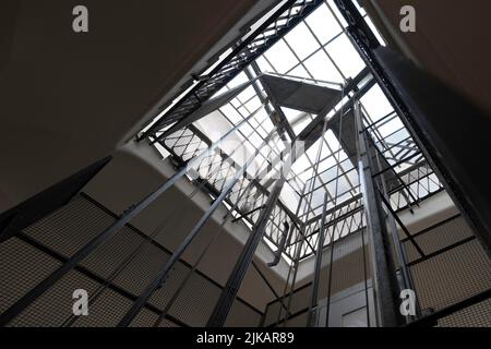 Dramatische Aufnahme eines Treppenhauses mit Blick auf einen Aufzugsschacht mit Metallstangen, Kabeln und Kabine in einem alten Apartmentgebäude. Enge Schärfentiefe Stockfoto