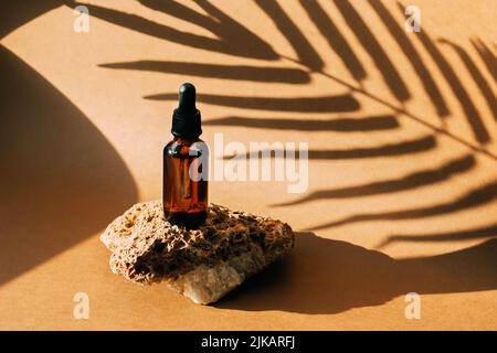 Kosmetische Tropfflasche Stein Podium Sockel. Brauner Hintergrund mit harten Schatten vom Pflanzenzweig Stockfoto