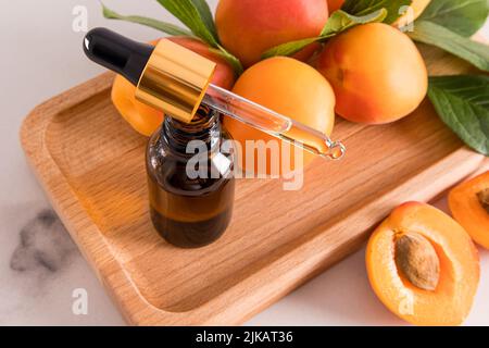 Auf einem Holztablett steht eine offene Flasche mit natürlichem Aprikosenkernöl oder organischem Selbstpflegeserum Stockfoto