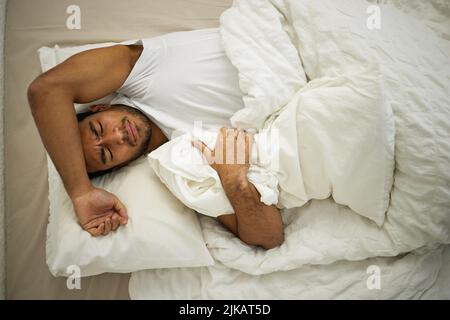 Ein junger Mann runzelte die Stirn, während er in seinem Bett lag. Stockfoto