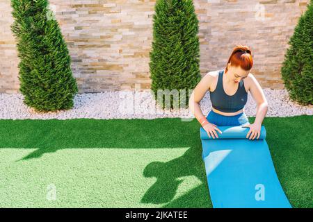 Attraktive junge Sportler. Schieben einer Yoga-Matte, um Entspannungsübungen durchzuführen, Vorbereitung für Dehnübungen. Konzept der Gesundheit und Wellness. Kopie Stockfoto