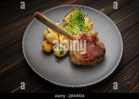 Kalbsentrecote mit Kartoffeln und Mais, auf einem Teller auf einem hölzernen Hintergrund Stockfoto