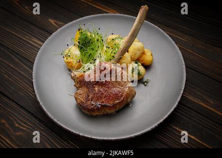 Kalbsentrecote mit Kartoffeln und Mais, auf einem Teller auf einem hölzernen Hintergrund Stockfoto