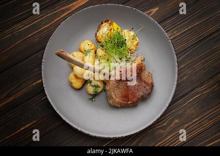 Kalbsentrecote mit Kartoffeln und Mais, auf einem Teller auf einem hölzernen Hintergrund Stockfoto